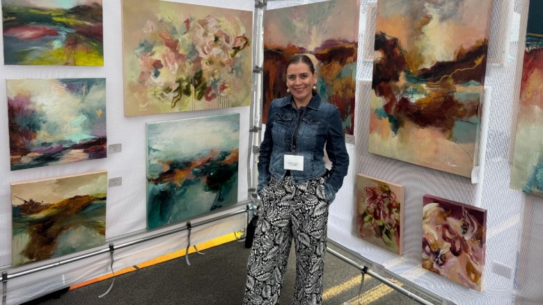 Woman standing in front of abstract paintings at an outdoor art display.