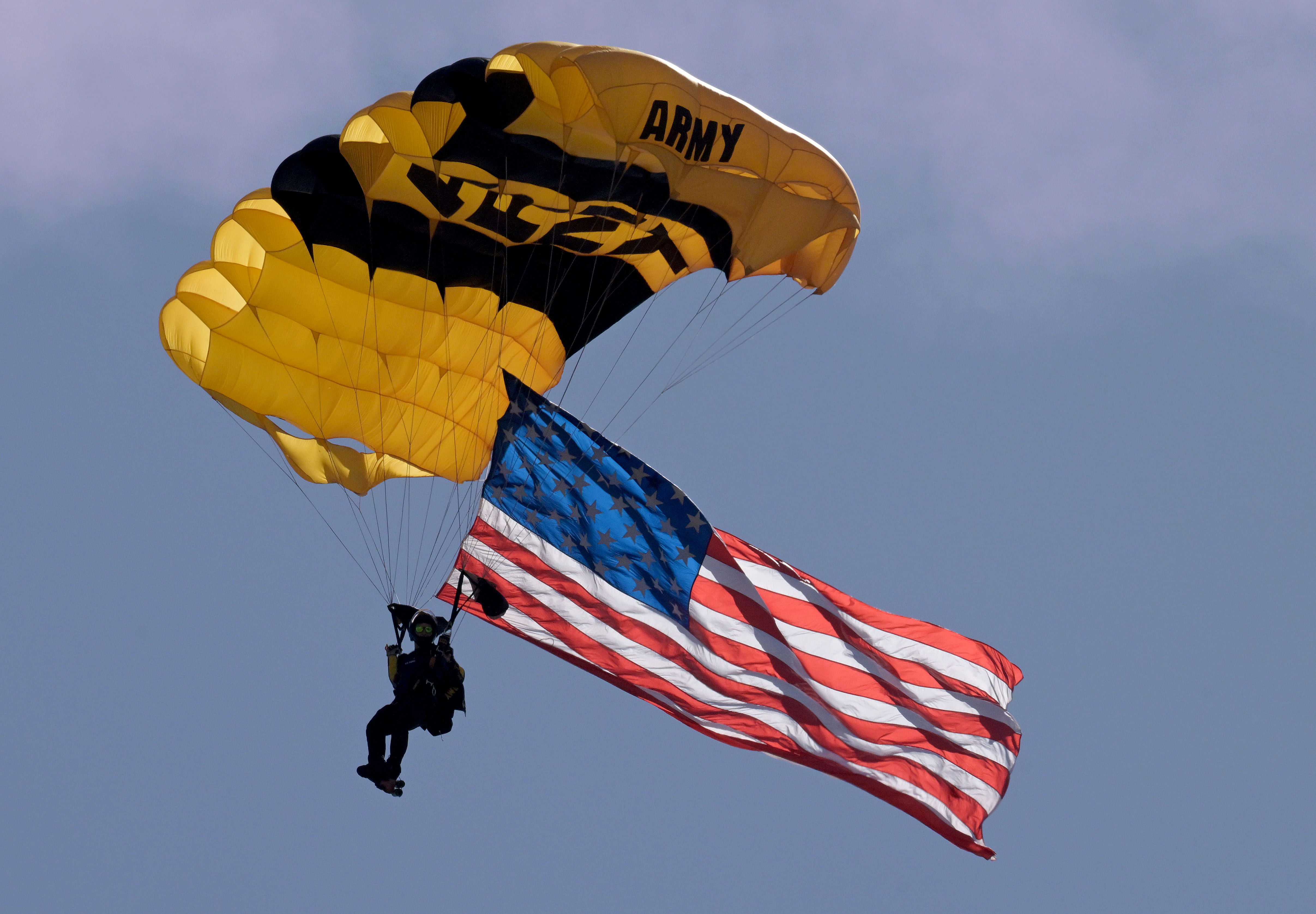 A United States Army paratrooper desends with the American Flag...