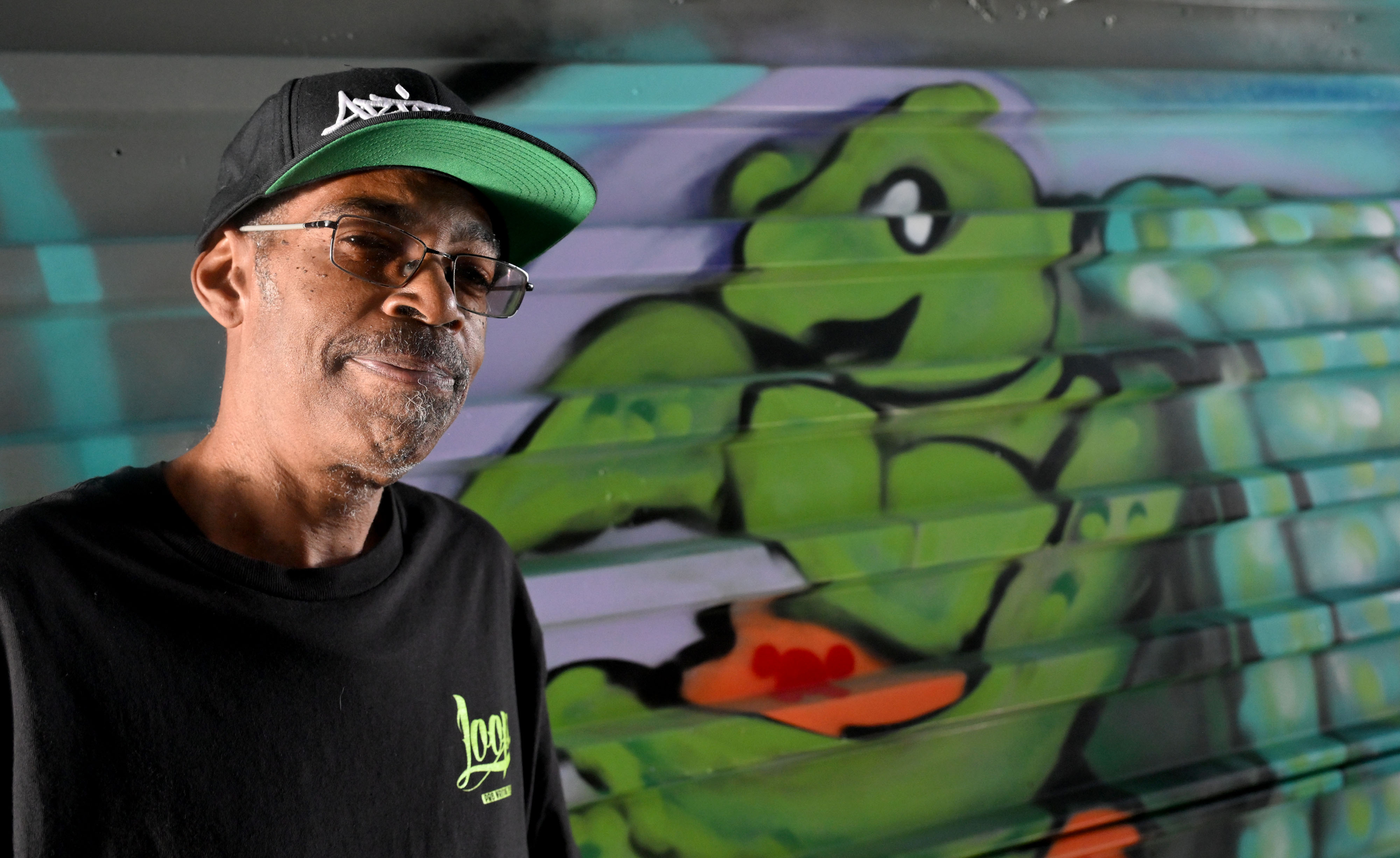 Artist, D. âZâ Brooks stands next to his mural of...