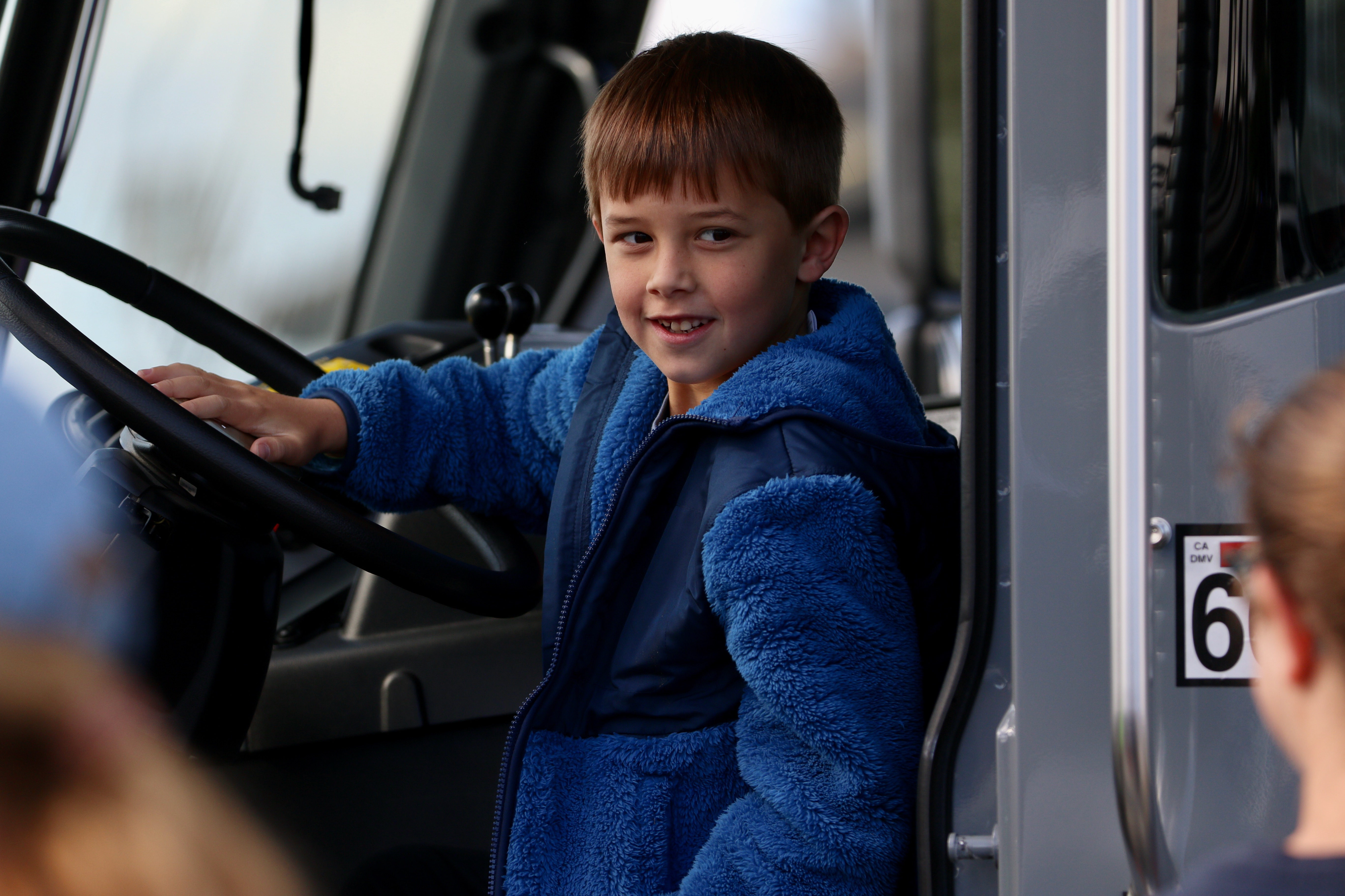 A boy poses for a picture inside a sanitation truck...