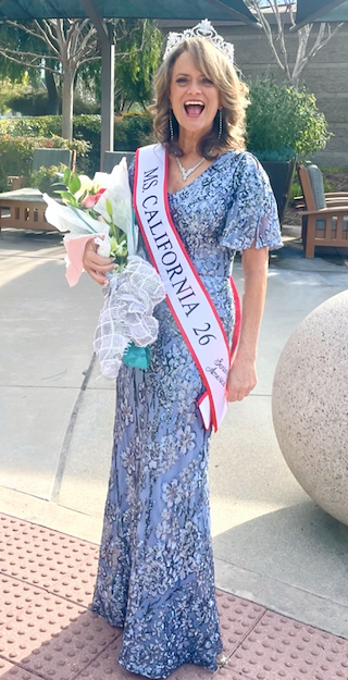 A woman in a ball gown with a crown, sash and flowers