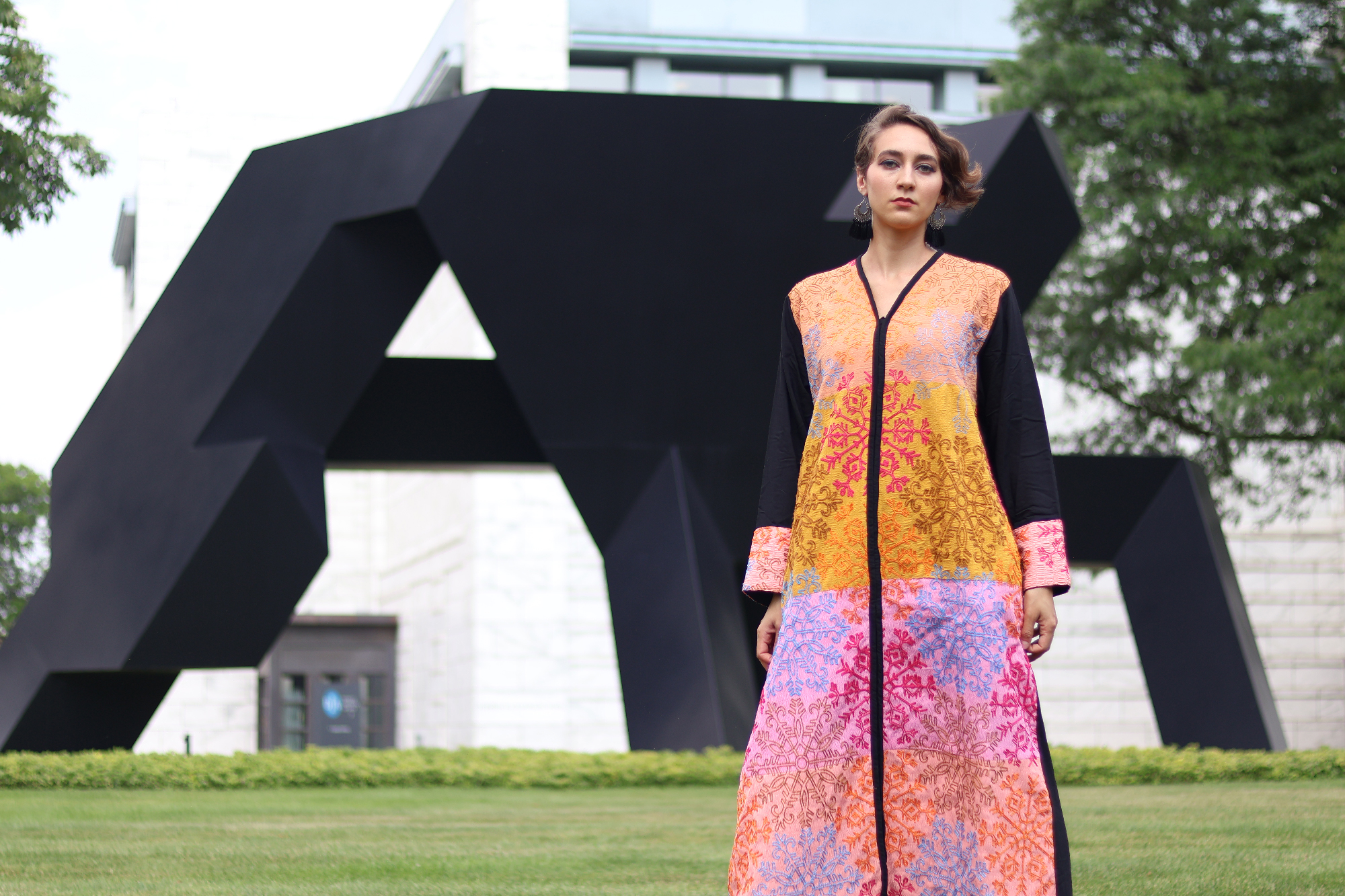 woman in colorful dress stands outside large black sculpture