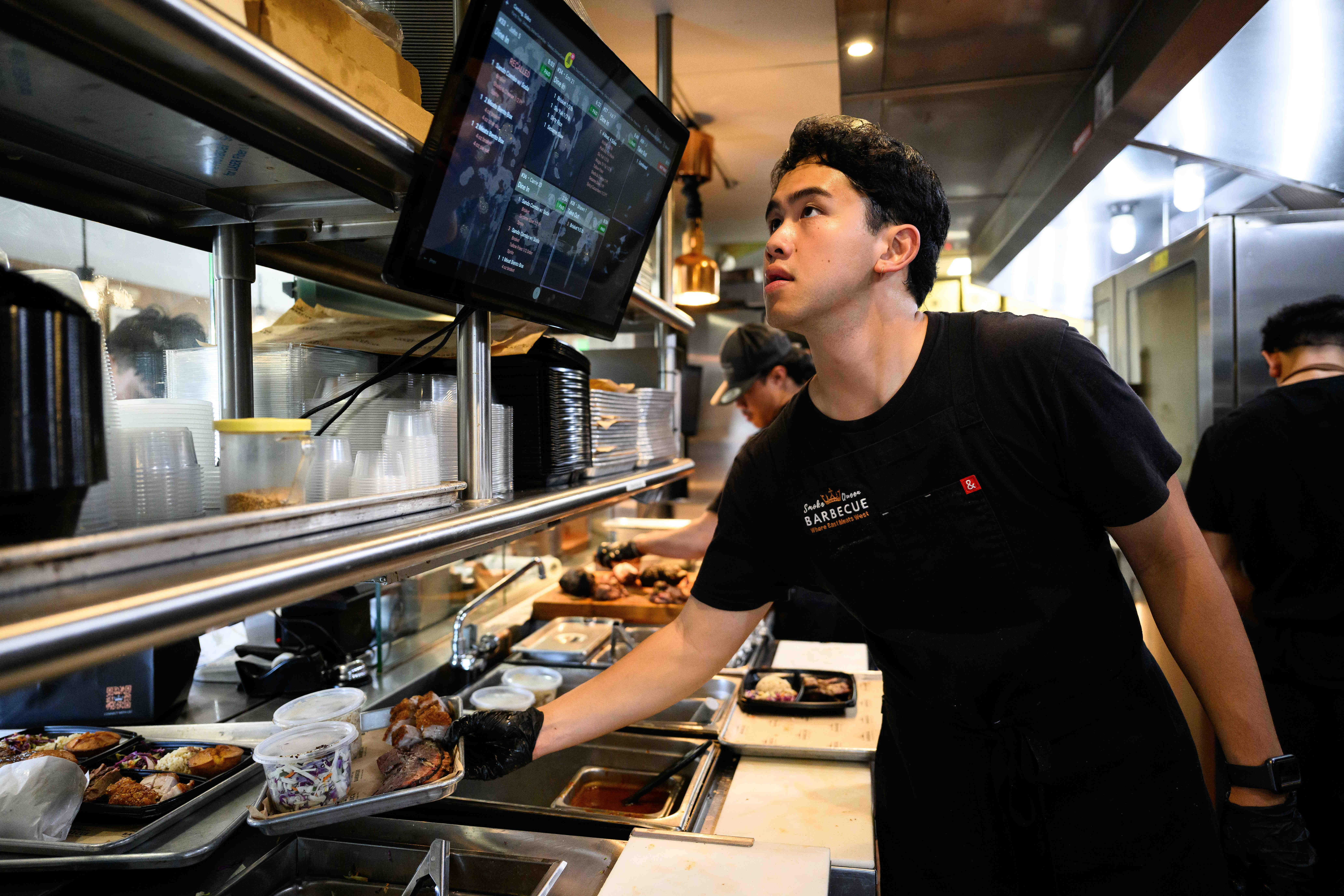 Workers prepare food in the kitchen at Smoke Queen Barbecue,...