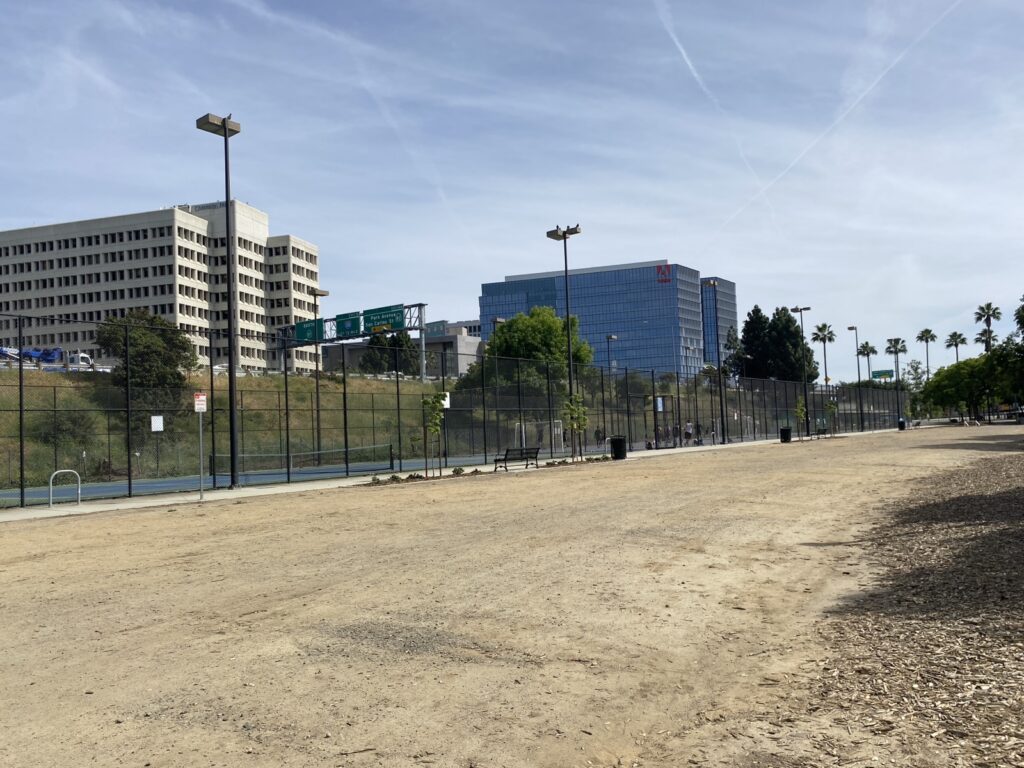 A dirt field with pickleball courts in the background.