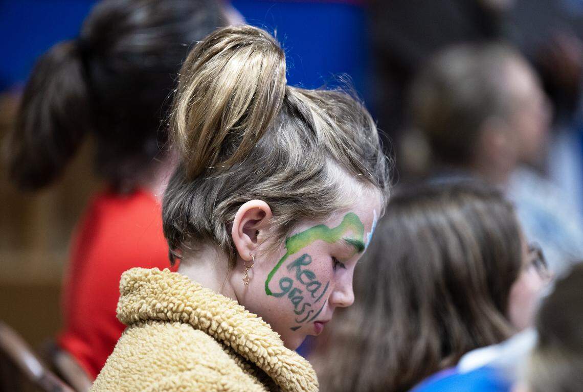 Matilda Rogus, a student at Crocker/Riverside Elementary School, wears face paint that says “real grass” in a silent protest against replacing the existing turf with artificial turf during a community meeting about the project on Tuesday.