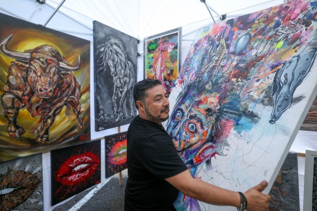 Artist Antonio Proa, from Tijuana, holds his painting depicting Spanish artist Salvador Dali, titled "Motivos Dali", as he looks for a spot to hang his multimedia painting at his booth during the Mission Fed ArtWalk in Little Italy in San Diego on Sunday, April 26, 2026. (Hayne Palmour IV / For The San Diego Union-Tribune)