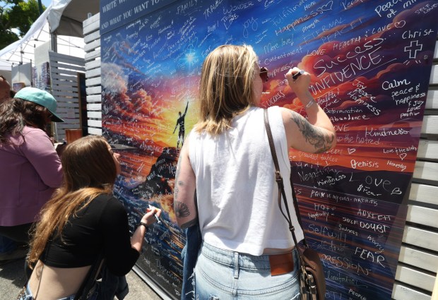 People write on a collaborative art project, called the Gemini Project, created by artists Geoff Pecoff and Stephanie Clair, where people can write down what they want to let go of and what they want, during the Mission Fed Art Walk in Little Italy in San Diego on Sunday, April 26, 2026. (Hayne Palmour IV / For The San Diego Union-Tribune)