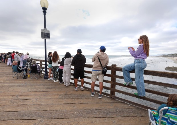 Spectators wait in and around the Oceanside Pier for a glimpse of the re-entry of Artemis II Friday. (John Gastaldo / For The San Diego Union-Tribune)