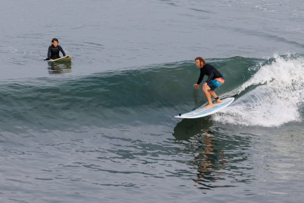 Imperial Beach resident Matt Henry rides a wave as his son Liam, 13, watches at the Imperial Beach Pier on Wednesday, March 25, 2026. (Kristian Carreon / The San Diego Union-Tribune)