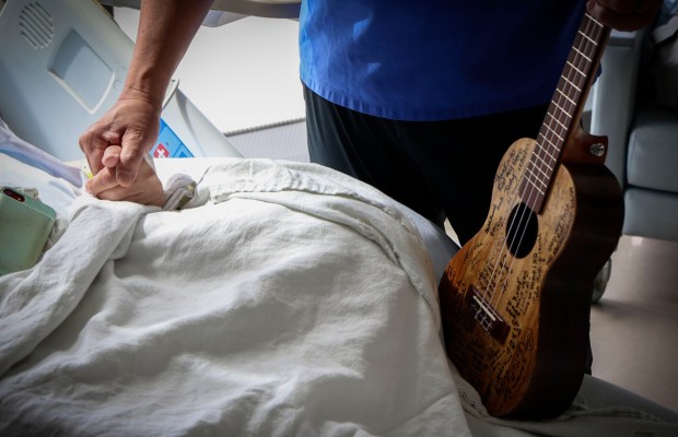 Nurse Rod Salaysay with his Ukulele for patient, holds patient Ruth Dennison's hand after playing her a song at UCSD Jacobs Medical Center in La Jolla on Wednesday, April 22, 2026. Salaysay has been singing to his patients for over Two decades and plans to retire later this year. (Sandy Huffaker / For The San Diego Union-Tribune)