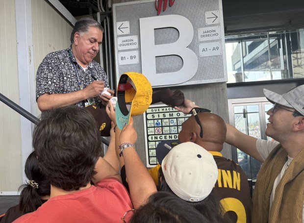Padres Spanish-language broadcaster Eduardo Ortega, left, signs autographs for fans before Sunday's Mexico City Series finale against the Arizona Diamondbacks in Mexico City. (Ryan Finley, U-T)