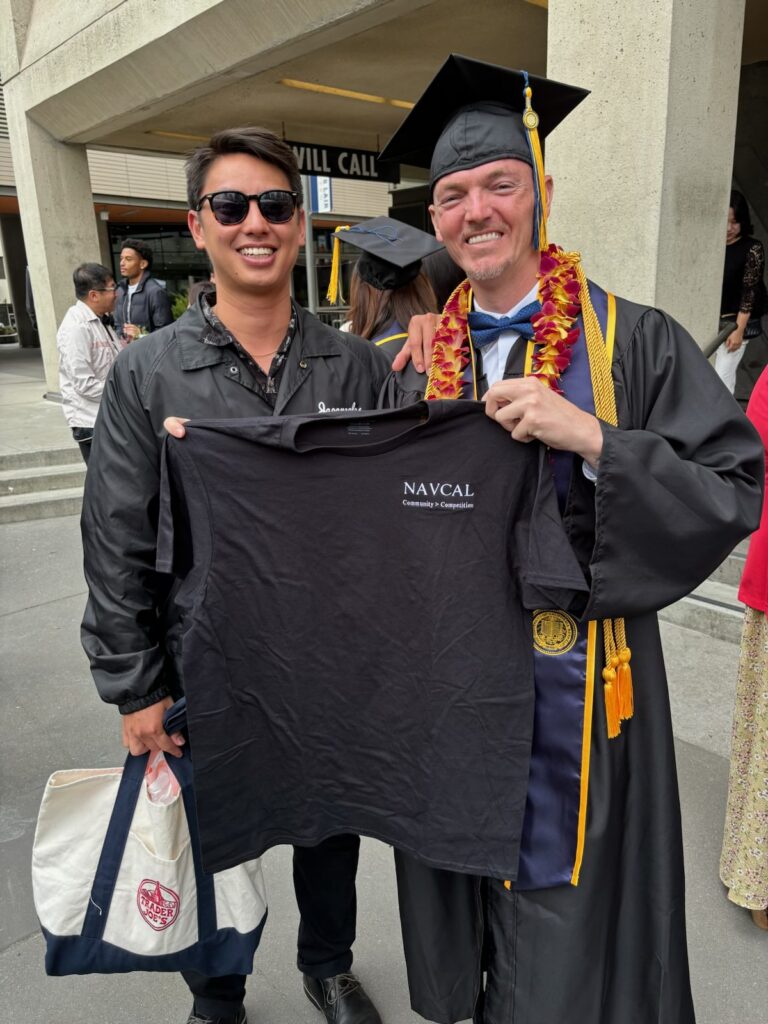 Dean Tanioka and Johnny Smith stand outside of Smith's graduation ceremony; they're holding a black NAVCAL T-shirt