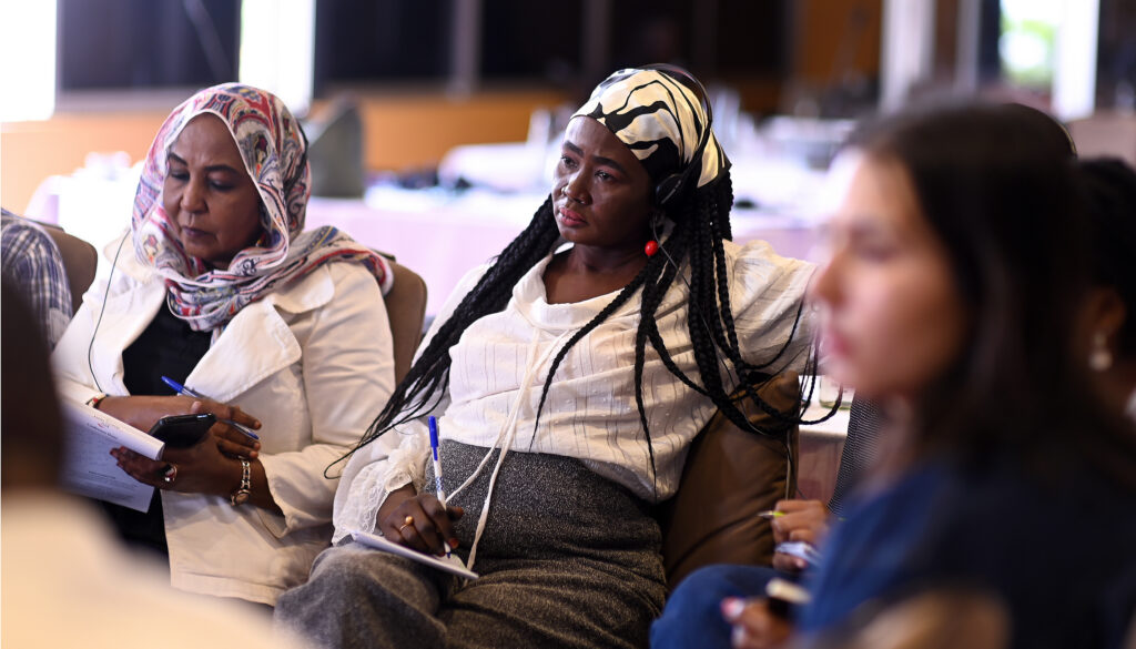 Three women, all seated, listen to a presentation
