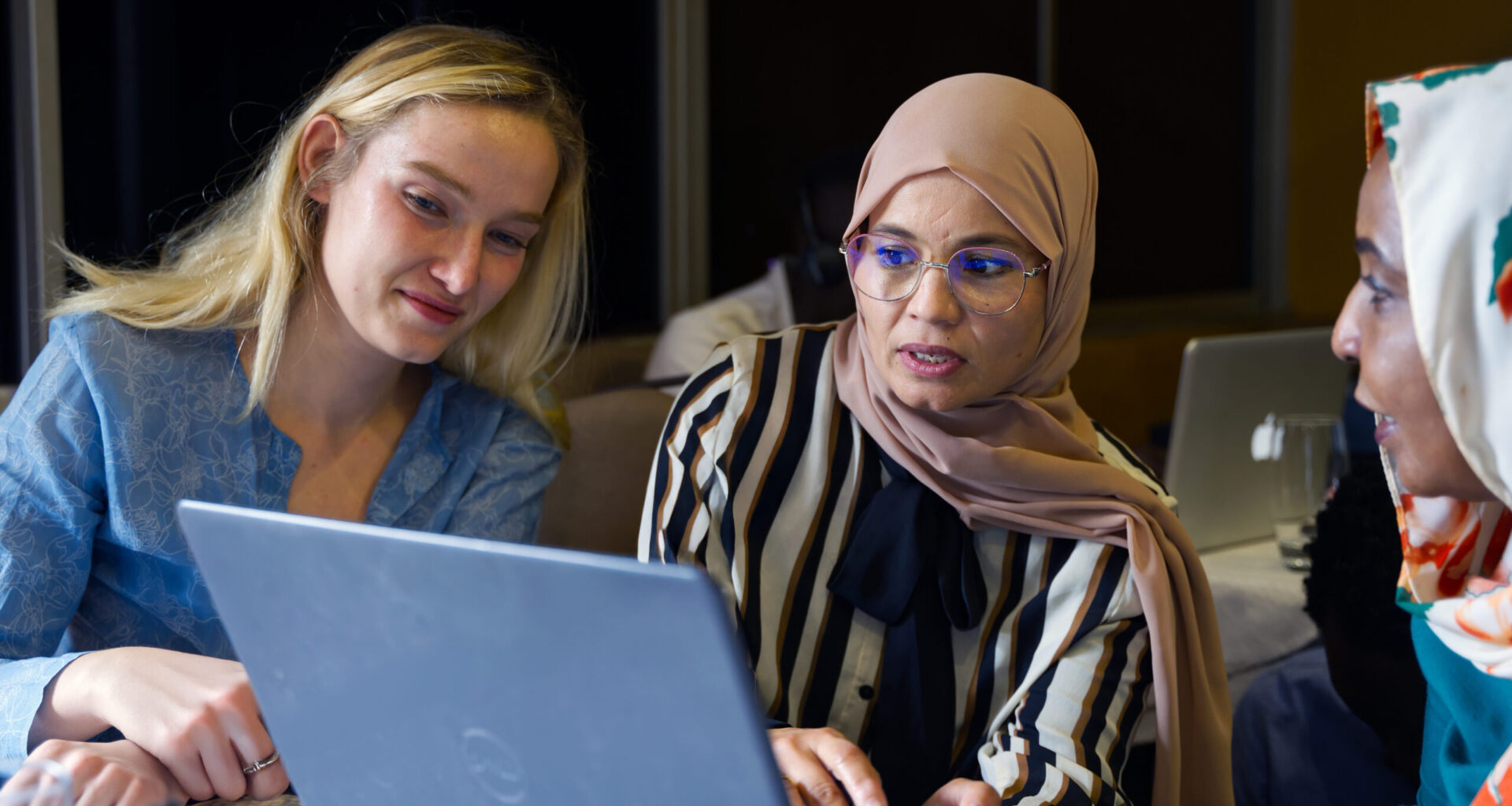 Three women sit before a laptop computer