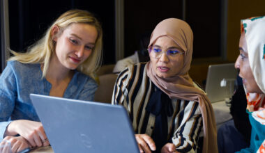Three women sit before a laptop computer