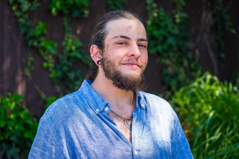 A man with a beard dressed in a collared, button-down shirt seen on a backdrop of green hedges. He has concerns about bathroom access as for people who are transgender.