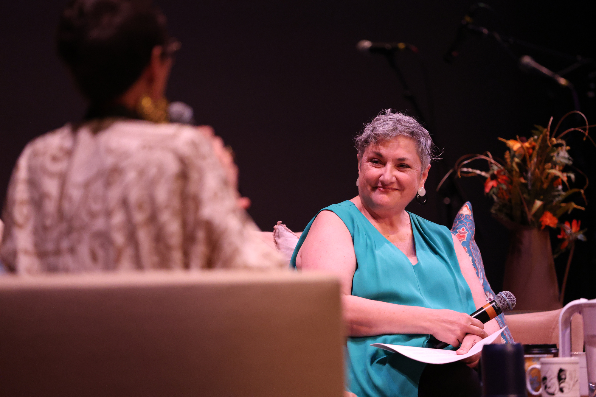 seated older woman faces interviewer, holds mic
