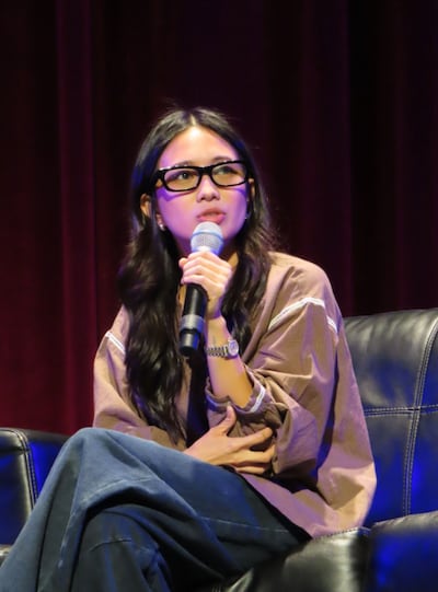 NIKI crosses her legs while speaking into a microphone.