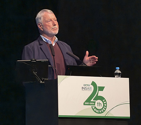David Amaral stands in a dark suit behind a podium on a stage, with a sign that states INSAR on the podium.