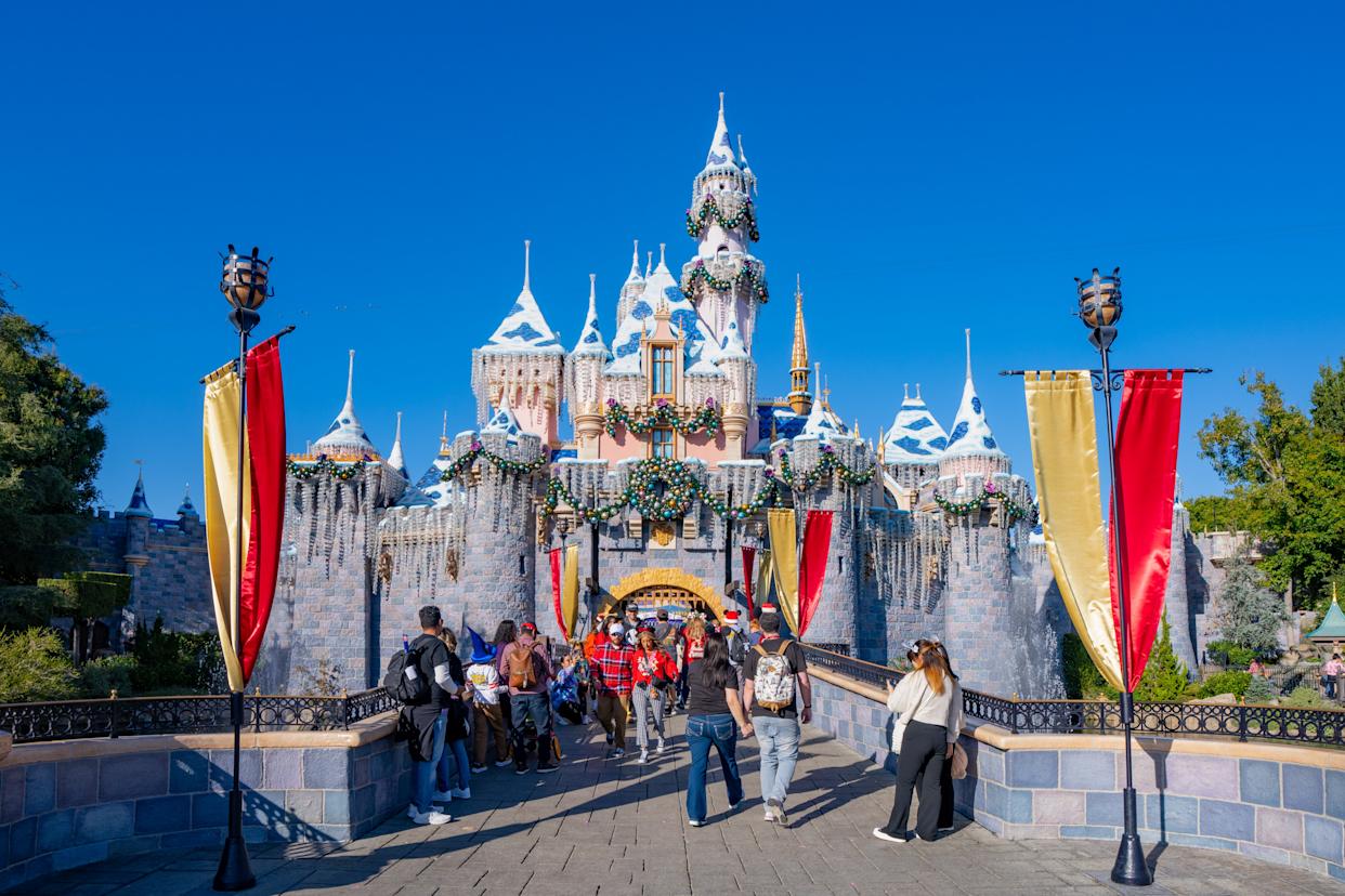 Sleeping Beauty Castle at Disneyland, decorated with Christmas ornaments, with visitors walking towards its entrance.