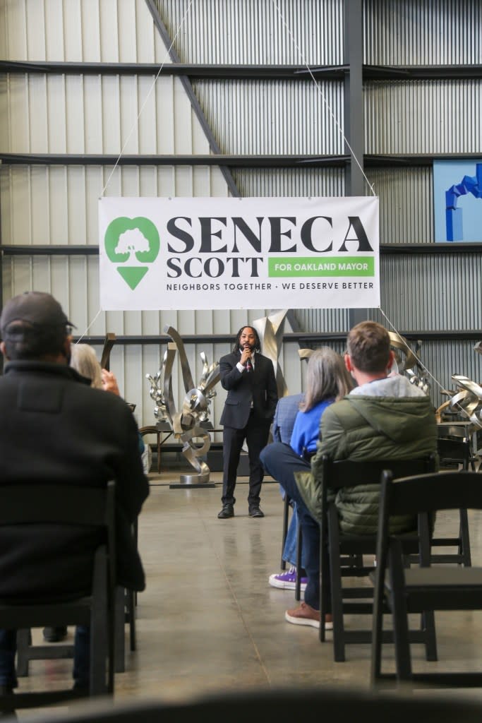Seneca Scott speaking at an event under a banner that reads “Seneca Scott for Oakland Mayor, Neighbors Together, We Deserve Better.” Seneca Scott