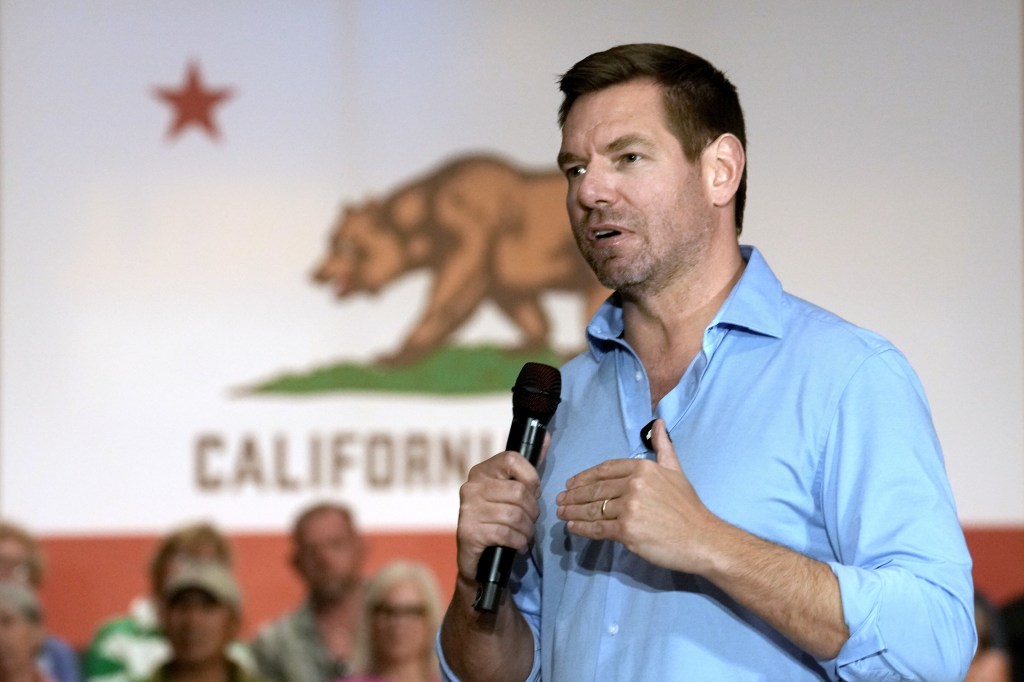 Rep. Eric Swalwell speaks at a town hall meeting in Sacramento, with the California state flag in the background.