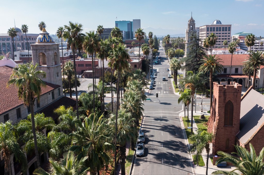 Aerial view of downtown Riverside, California, with a street lined with palm trees leading to city buildings and a church.