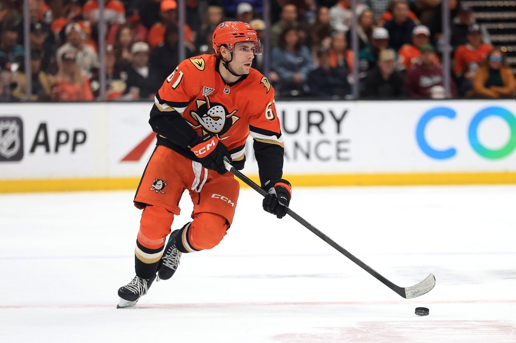 Anaheim Ducks player Cutter Gauthier in an orange uniform controls the puck during a game against the Vancouver Canucks.