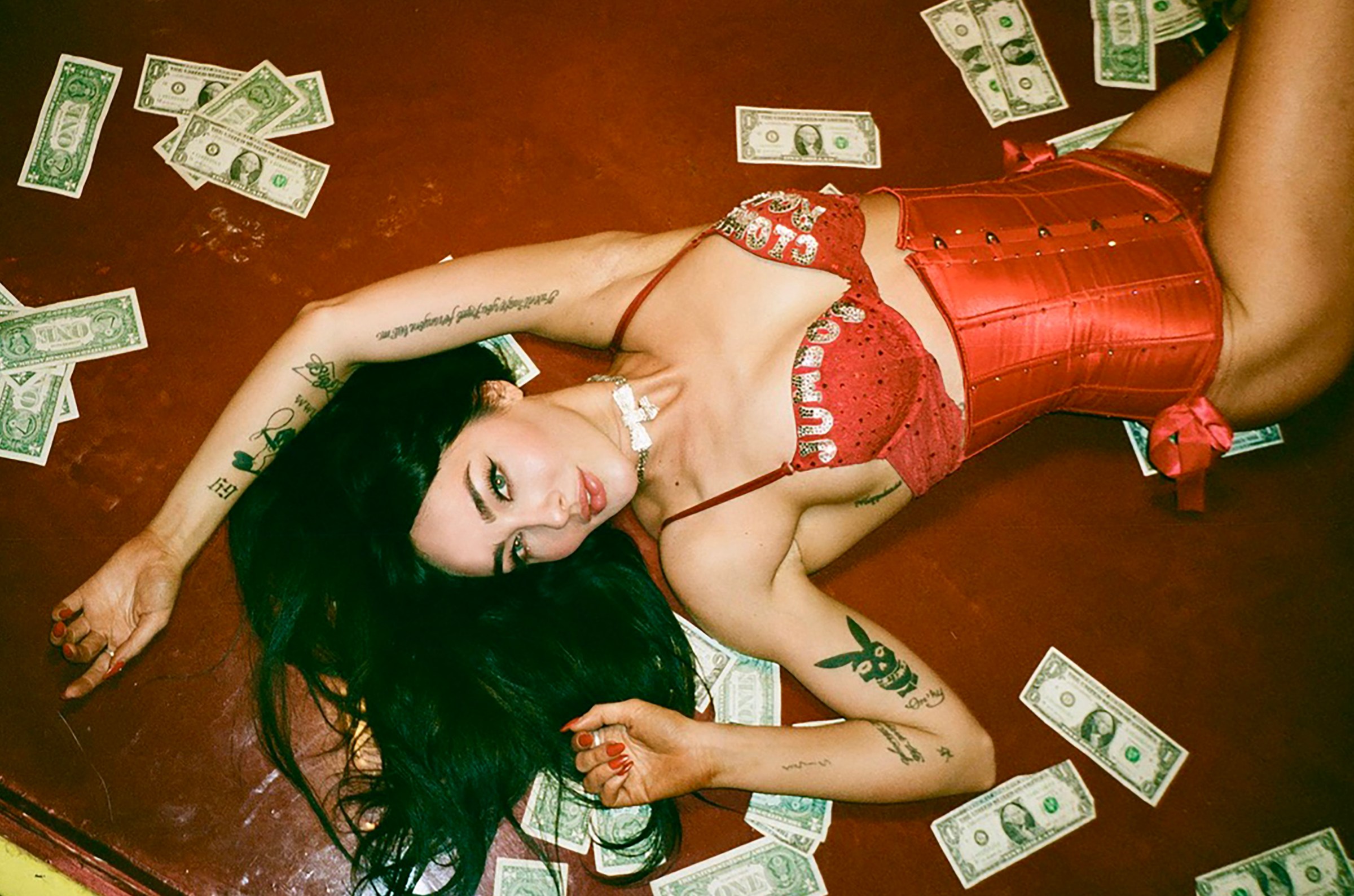 Overhead shot of Scarlett Kapella lying on a red table with bills around her.