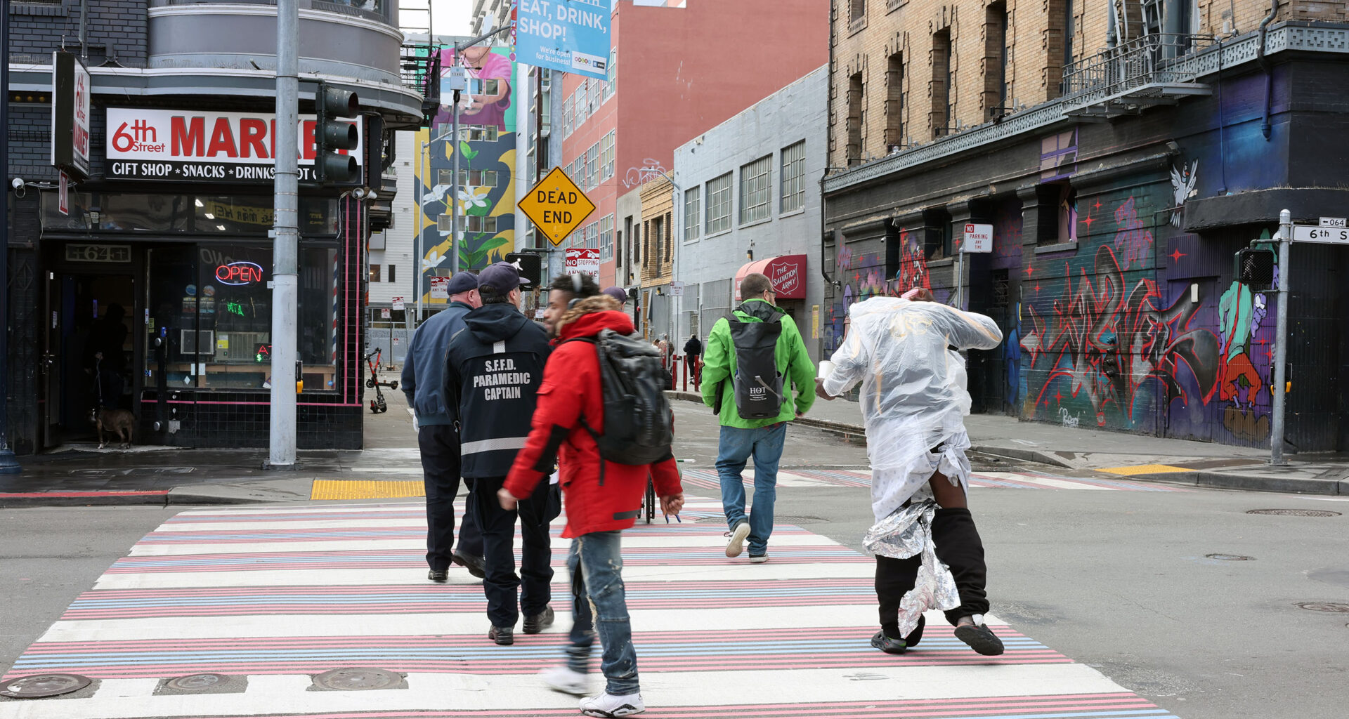Amidst the vibrant cityscape, people cross the street, one draped in reflective material, reminiscent of a triage blanket. The backdrop of colorful buildings and dynamic street art adds an artistic flair to the urban scene.