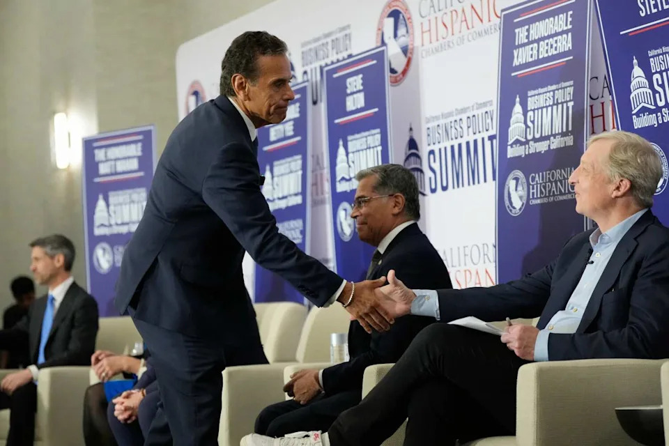 A standing man shakes hands with a seated man.