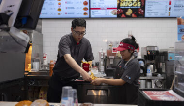 Two fast food workers in grey polos and black pants filling a Wendy's bag with food at a Wendy's location.
