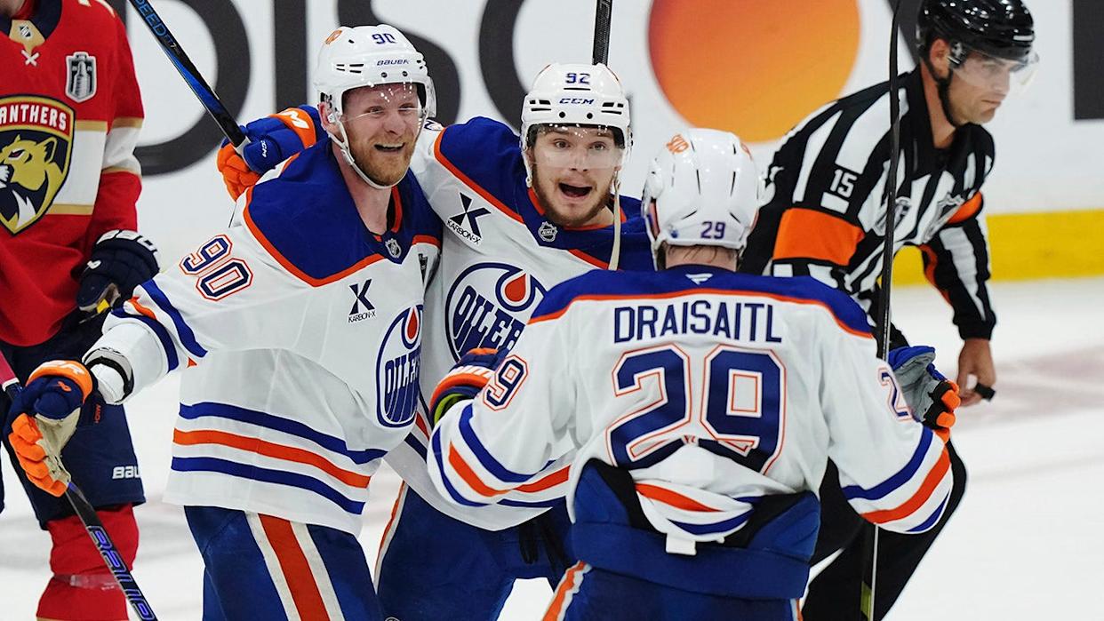 Vasily Podkolzin celebrating goal with Corey Perry and Leon Draisaitl as Niko Mikkola watches during hockey game