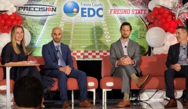 four people seated on a stage with a football stadium backdrop with balloons