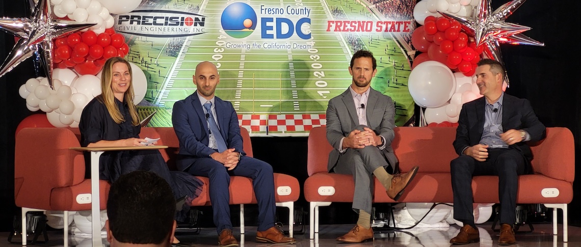 four people seated on a stage with a football stadium backdrop with balloons