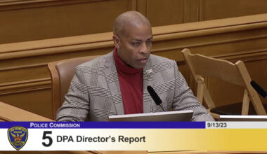 A man in a suit sits at a desk in a courtroom.