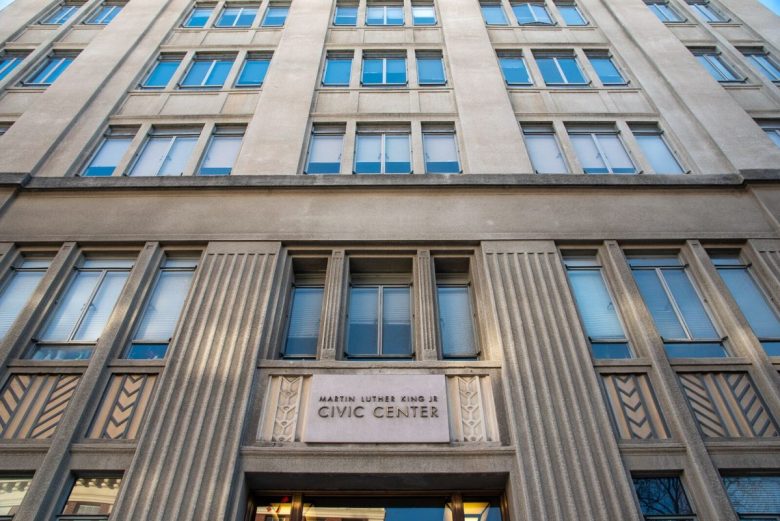 A view looking up at Berkeley City Hall, a five-story grey government building, from the sidewalk.