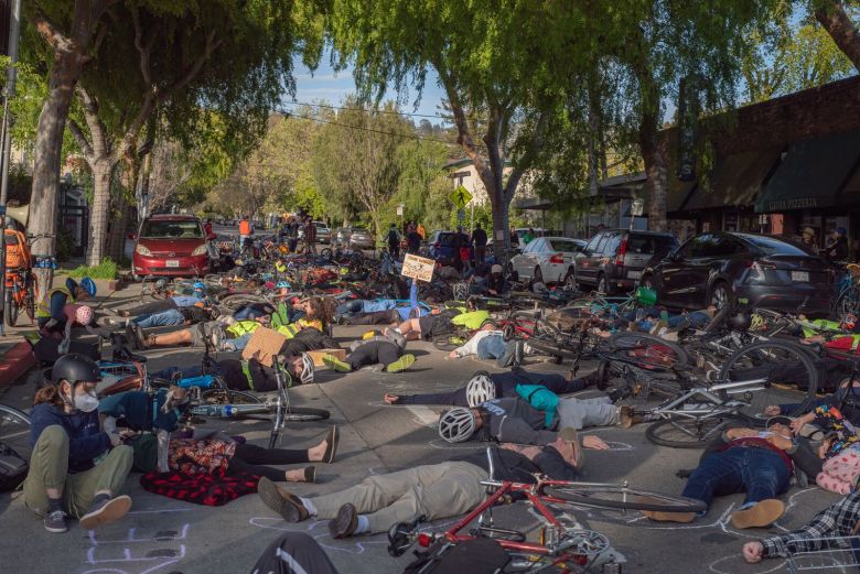 Dozens of people lie with their bicycles on the pavement of Hopkins Street. One holds a sign calling for street safety improvements.
