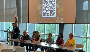 MC and panelists sitting at a table facing attendees
