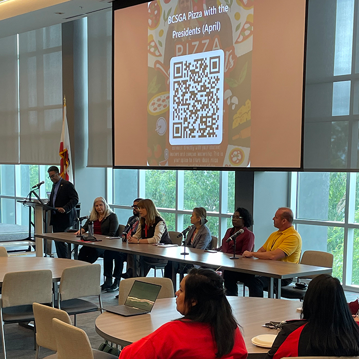 MC and panelists sitting at a table facing attendees
