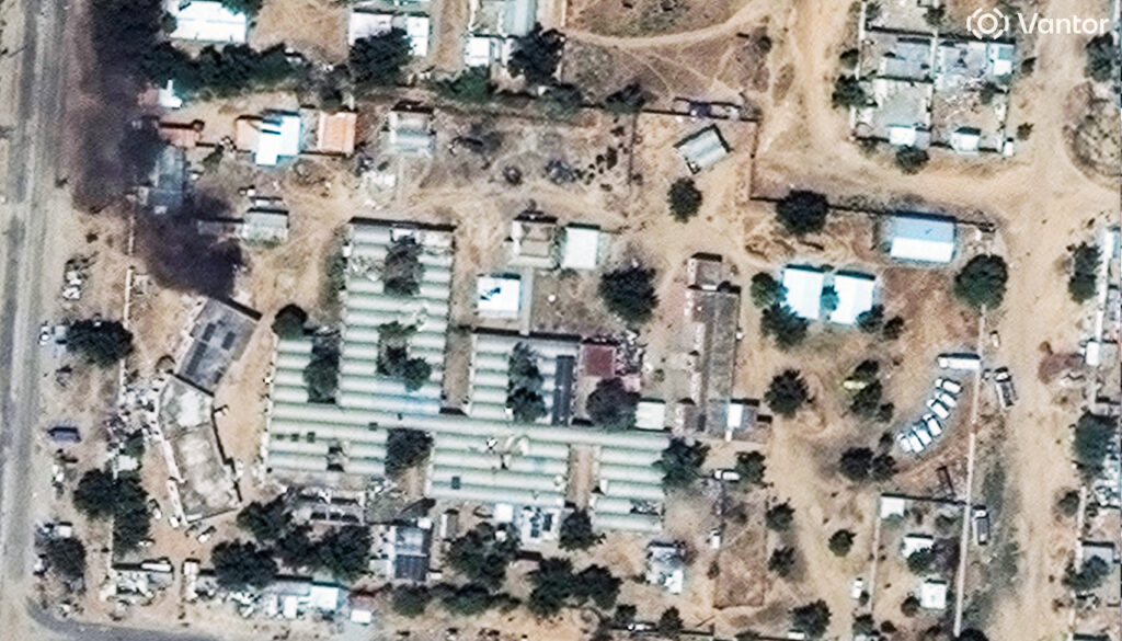 A satellite image showing sandy roads and varied buildings and vehicles in el Fasher, one of the largest cities in Sudan's Darfur region. Black smoke rises from the grounds of a hospital in the upper left corner.