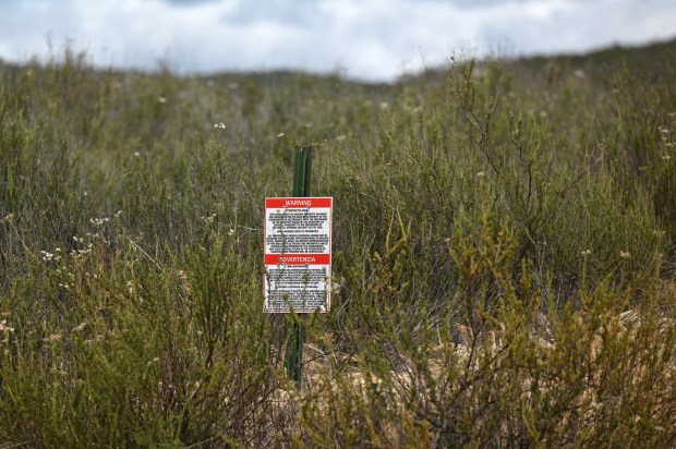 A warning sign on the US-side of the border viewed from Tecate, Mexico by the US Department of Defense, about arrest if territory is trespassed during a "ceremony" rally against the destruction of the Kuchamaa Mountain left by the construction of a new border wall at the US-Mexico Border in Tecate, Baja California, Mexico on Sunday, April 12, 2026. (Carlos Moreno / The San Diego Union-Tribune)