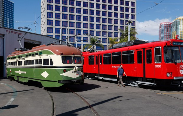 MTS project coordinator Alfonso Florian walks by a restored 1946 Presidents Conference Committee (PCC) streetcar, left, and the first red San Diego Trolley, the 1001, which are part of the Silver Line's vintage vehicles fleet on March 9, 2026, in San Diego. (K.C. Alfred / The San Diego Union-Tribune)