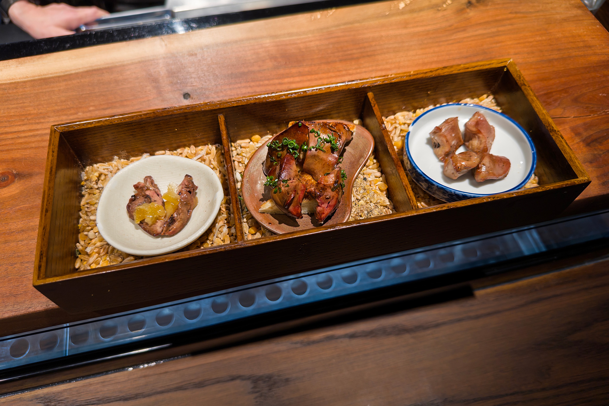 A trio of grilled chicken offal served in an elegant wooden box.