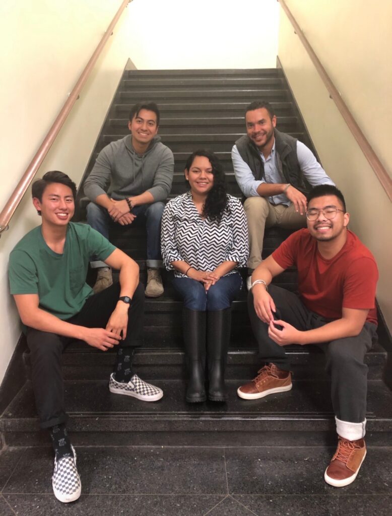 A group of five people who were part of the 2018 Teach In Prison facilitation team seated in a stairwell, smiling for a photo