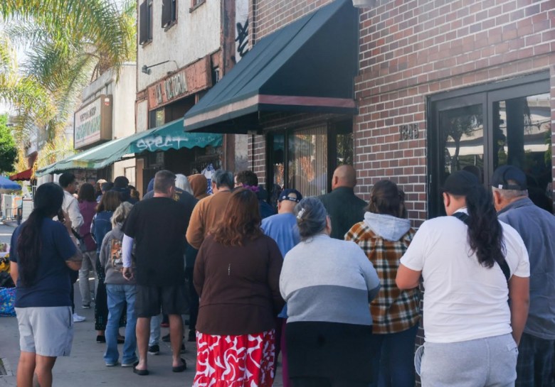 Several people stand in a line that three storefronts outside a popular Mexican restaurant.