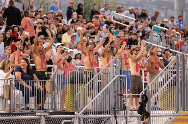 Many fans fill the stands while several stand in front of a railing with no shirts on, each with one letter on their chests, spelling out "Growlers."