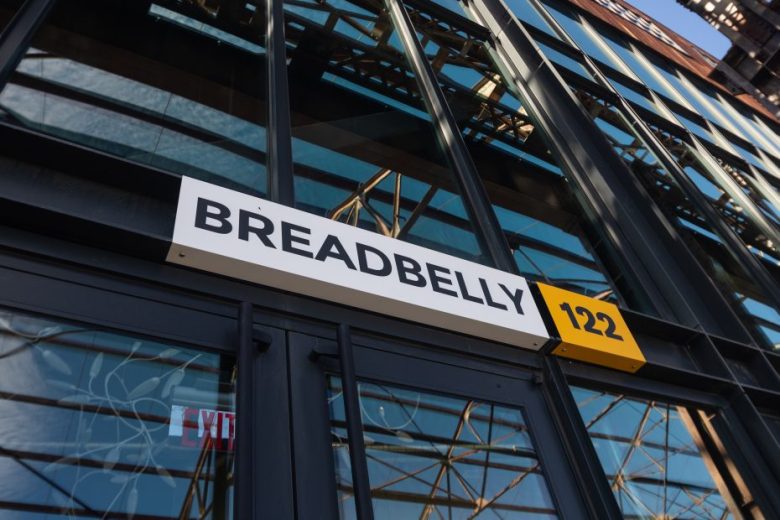 Exterior of a building with large windows, featuring a white "BREADBELLY" sign and a yellow "122" sign above the entrance.