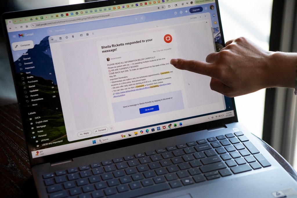A close-up shot of a person's hand pointing towards a computer screen displaying an email on a laptop on a small table in a restaurant.