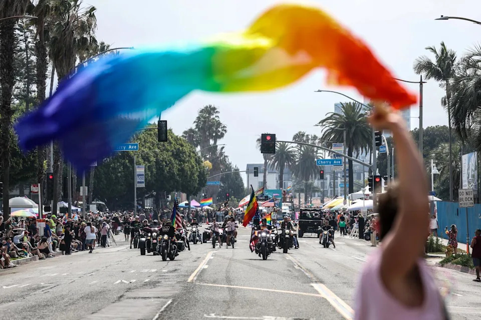 A rainbow flag frames motorcyclists in the parade.